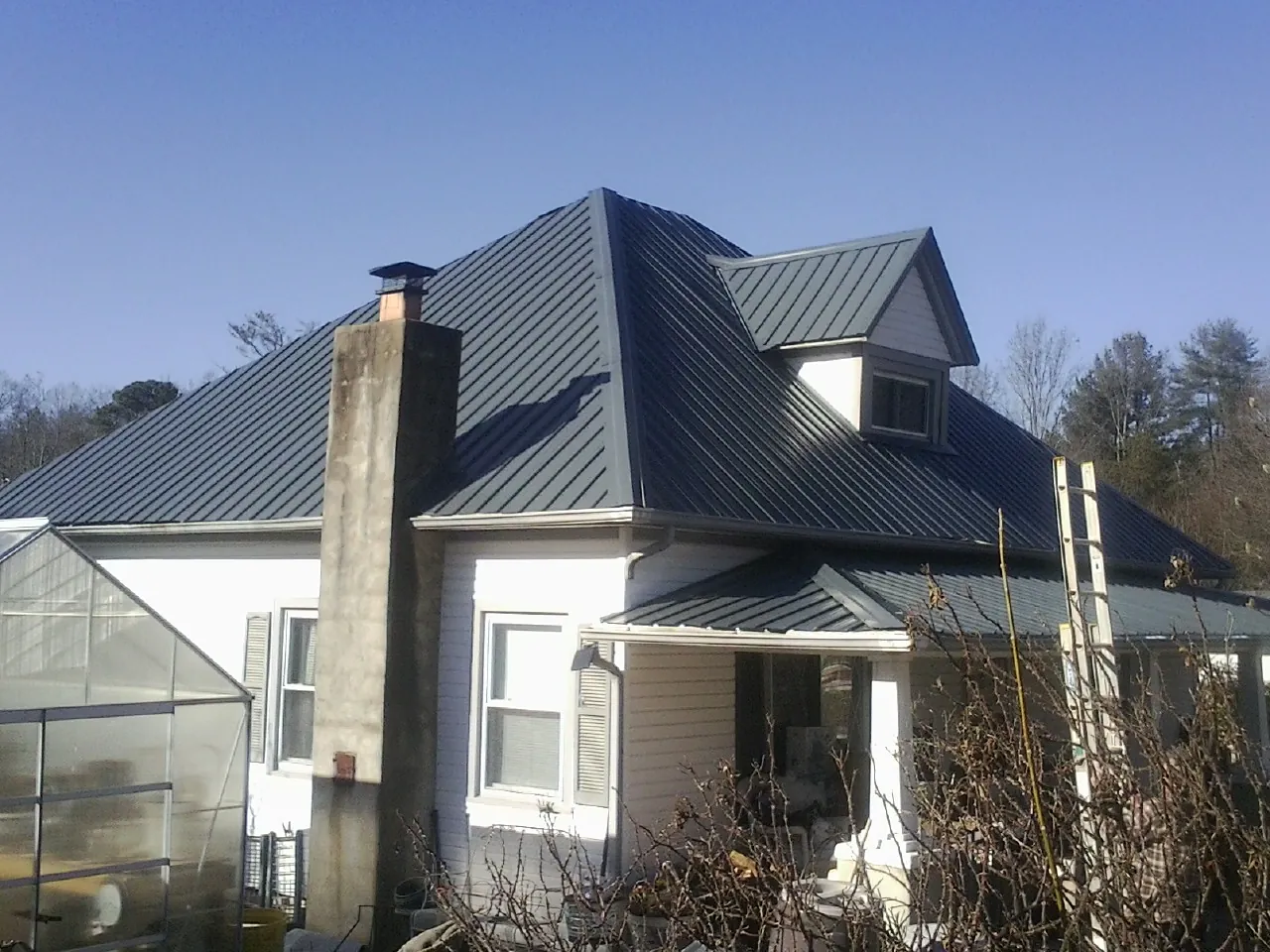 Dark blue standing seam metal roof on a white farmhouse with dormer in Clemson
