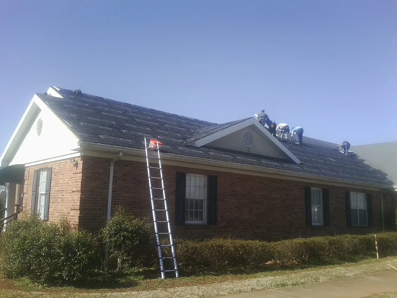 Crew tearing shingles off a brick ranch roof with a ladder set — Emergency Roof Repair work by our crew in Clemson
