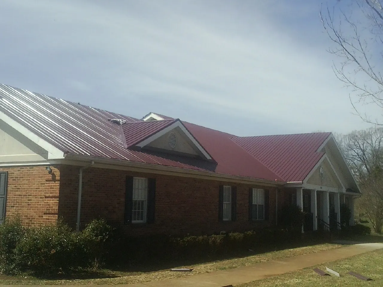 Red metal roof with gabled entries on a long brick building, from a Hail Damage Roof Repair job in Clemson