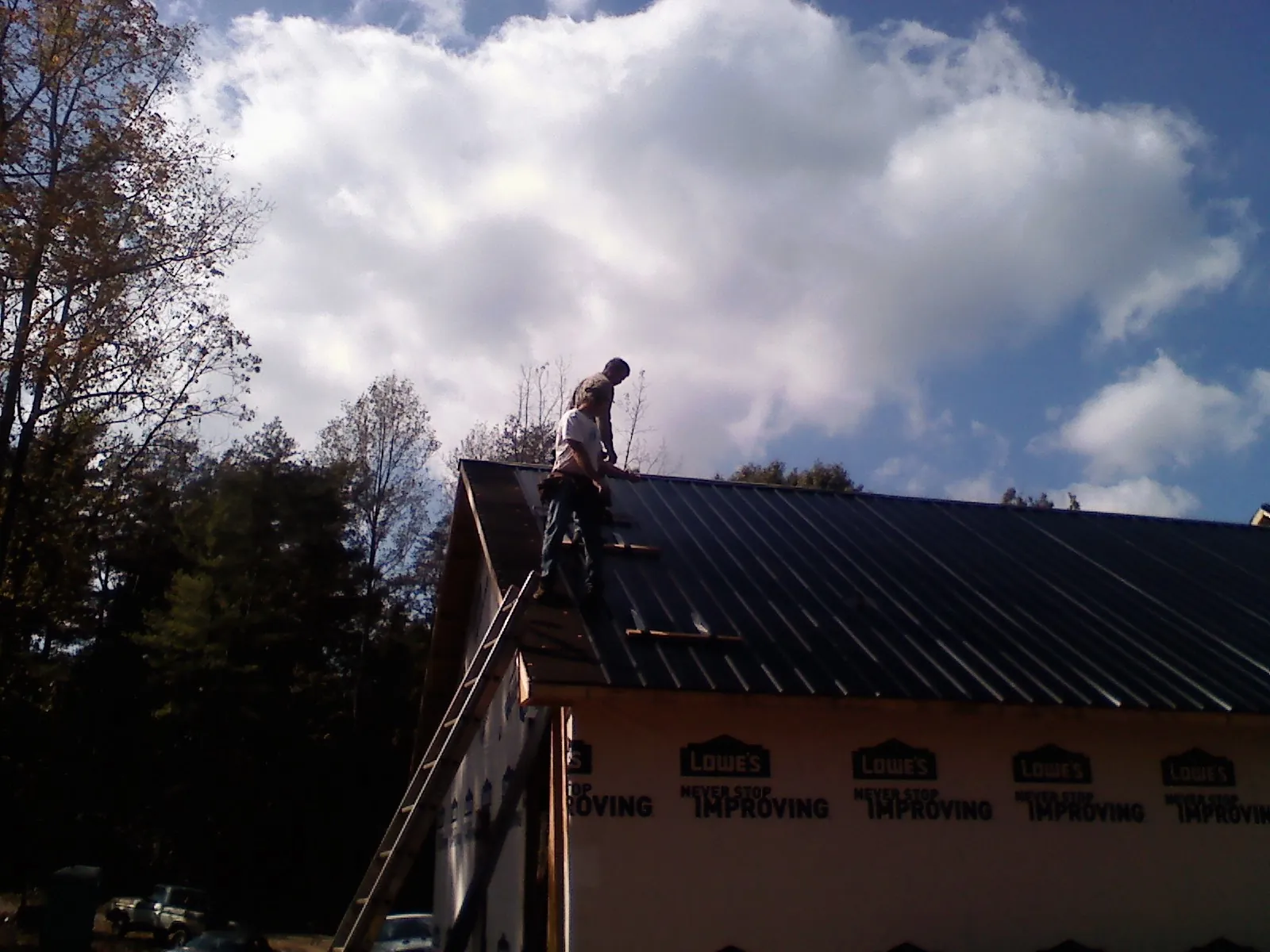 Roofer fastening dark metal panels high against a cloudy sky, from a Roof Inspection job in Clemson